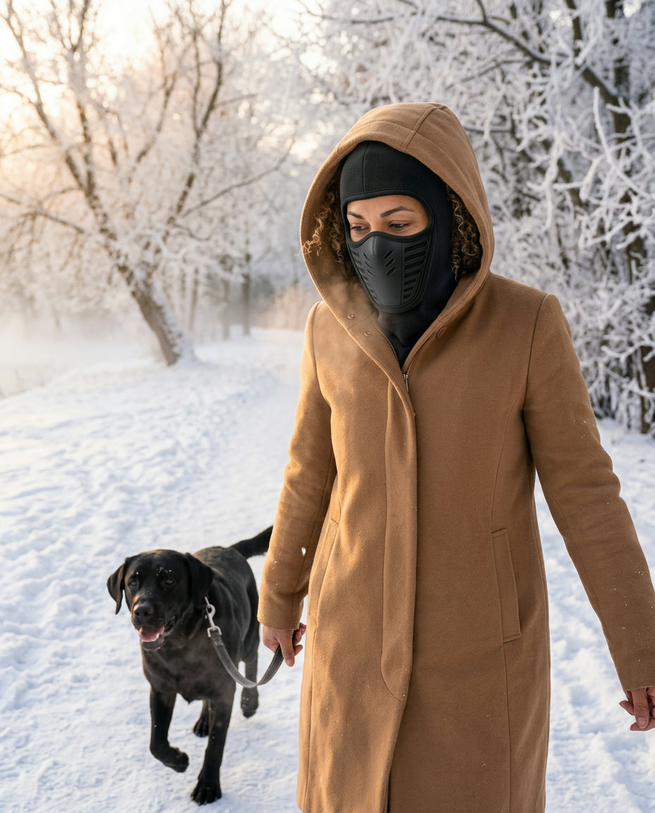 Woman walking a black labrador on a snowy park path wearing the vented fleece balaclava